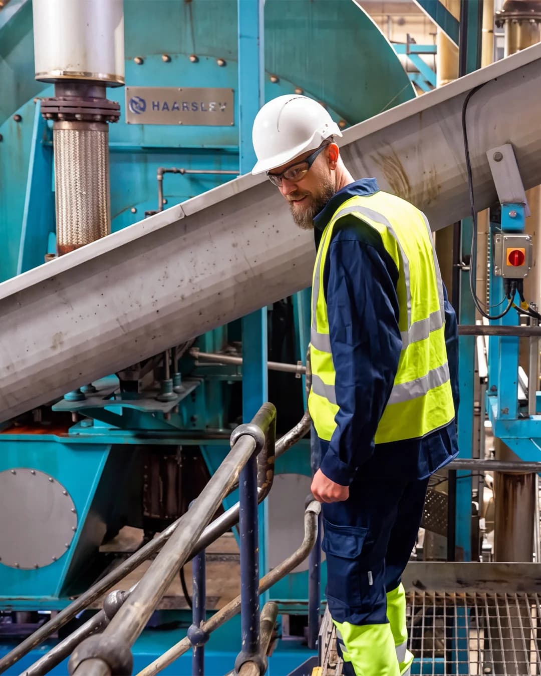 Haarslev Automation Manager at Haarslev, on the plant floor at Advanced Proteins. He stands on a walkway beside Haarslev process equipment, with an inclined screw conveyor running overhead.